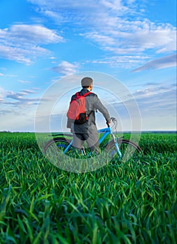 A businessman looks into the distance, he is standing with a backpack and a bicycle on a green grass field, dressed in a business