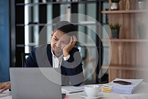 A businessman looks tiredly at a computer monitor and feels hopeless. A young man in a suit works in the office.