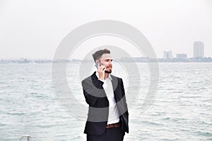 Businessman on luxury yacht with smartphone, handsome man wearing white shirt and suit on boat