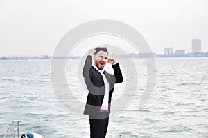 Businessman on luxury yacht with smartphone, handsome man wearing white shirt and suit on boat