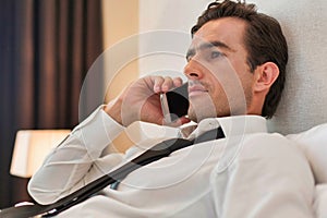 Businessman lying in bed while talking on smartphone