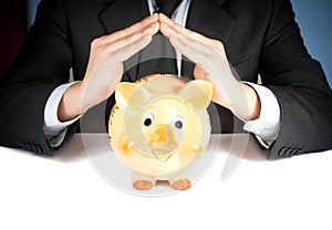 A businessman make with his hand a home behind a piggy bank, concept for business and save money