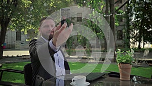 Businessman makes selfie during coffe break. Outdoor. Steadicam shot.