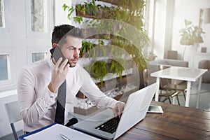 Businessman making a call and working on laptop in the office