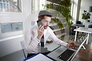 Businessman making a call and working on laptop in the office