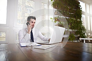 Businessman making a call and working on laptop in the office