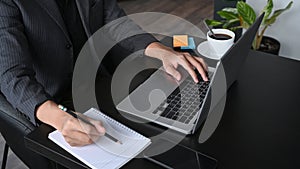 Businessman making notion notebook and using laptop at office desk.