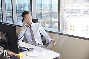 Businessman Making Phone Call Sitting At Desk In Office