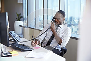 Businessman Making Phone Call Sitting At Desk In Office