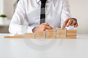 Businessman making stairs of wooden pegs in a conceptual image