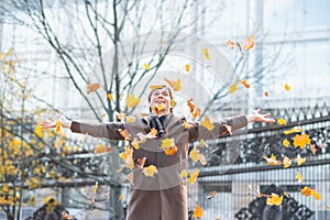 A businessman man in a coat threw yellow maple leaves, spreading his arms to the sides in the city square and smiling
