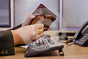 A businessman man with an empty wallet without money in his hands is working on a computer keyboard at an office desk, close-up