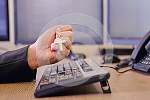 A businessman man with a religious Catholic cross in his hands is working on a computer keyboard at an office desk, close-up