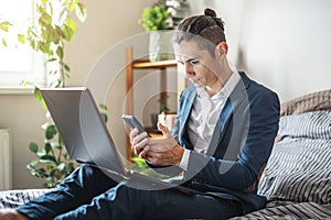 Businessman man in a suit is working remotely on a laptop in bed at home. Adapting to work during a pandemic