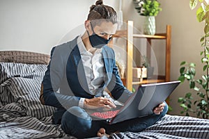 Businessman man in a suit is working remotely on a laptop in bed at home. Adapting to work during a pandemic