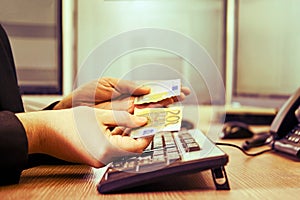 A businessman man with torn euro money in his hands is working on a computer keyboard at an office desk, close-up