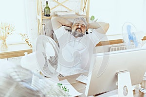 Businessman, manager in office with computer and fan cooling off, feeling hot, flushed