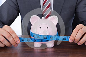 Businessman measuring piggybank with measure tape