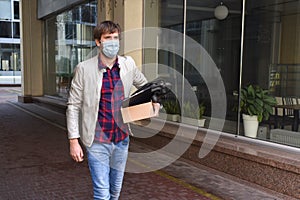 Businessman in a medical mask with a box of things leaving the business. An office worker lost his job due to the economic crisis