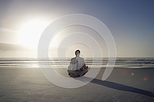 Businessman Meditating In Lotus Position On Beach
