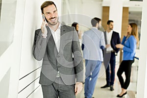 Businessman with mobile phone in office while other business people talking in background