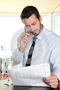 Businessman with mobile reading the newspaper, paused at the bar