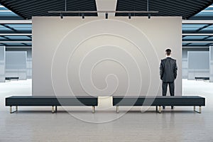 Businessman in modern gallery interior looking on blank wall