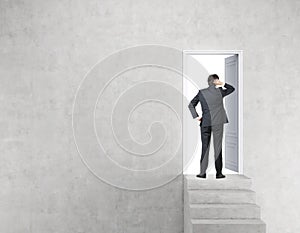 Businessman near open door in concrete wall with stairs