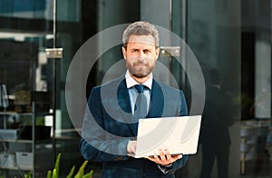 Businessman with notebook outdoor. Confident business expert. Handsome man in suit holding laptop against office