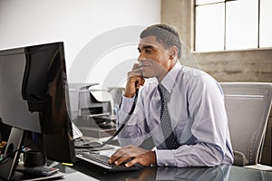 Businessman at an office desk using phone and computer