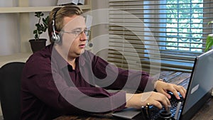 Businessman in the office on the phone, headset and data input to a laptop.