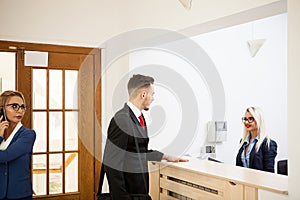 Businessman in office reception area talking with secretary
