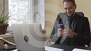 Businessman in office sending messages with mobile phone smiling