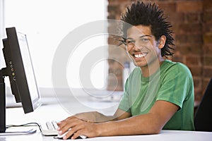 Businessman in office typing on computer smiling