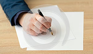 Businessman in the office writes a letter or signs a document on a piece of white paper with a fountain pen with nib.