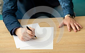 Businessman in the office writes a letter or signs a document on a piece of white paper with a fountain pen with nib.