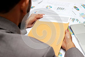 Businessman open brown envelope for evaluating business report, examining report papers on table in office.