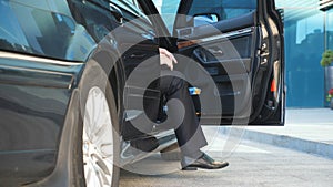 Businessman opens door and get out from the car near modern office building. Young business man uncover door of