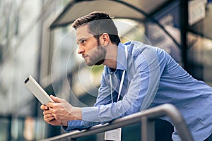 Businessman is outside of his job and he is using a tablet to work from it