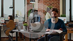 Businessman in pain wearing cervical collar and working on data report
