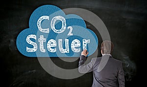 Businessman paints CO2 Steuer in german carbon tax on blackboard with chalk