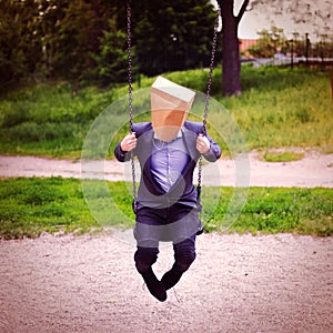 Businessman with paper bag on the head in the swing