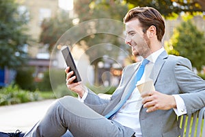 Businessman On Park Bench With Coffee Using Digital Tablet