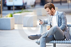 Businessman On Park Bench With Coffee Using Mobile Phone