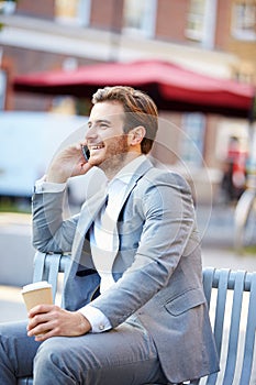 Businessman On Park Bench With Coffee Using Mobile Phone