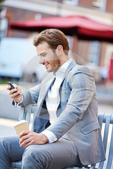 Businessman On Park Bench With Coffee Using Mobile Phone