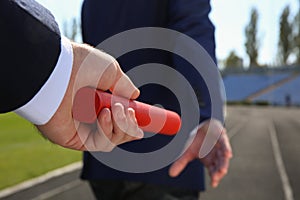 Businessman passing baton to his partner outdoors, closeup