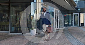 Businessman, phone call and walking with suitcase in city for conversation, travel or work trip outside building. Man or