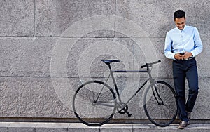 Businessman, phone and happy with bicycle by wall outdoor on sidewalk for text message and communication. Professional