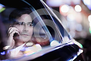 Businessman on the phone and looking out the car window at night, reflected lights